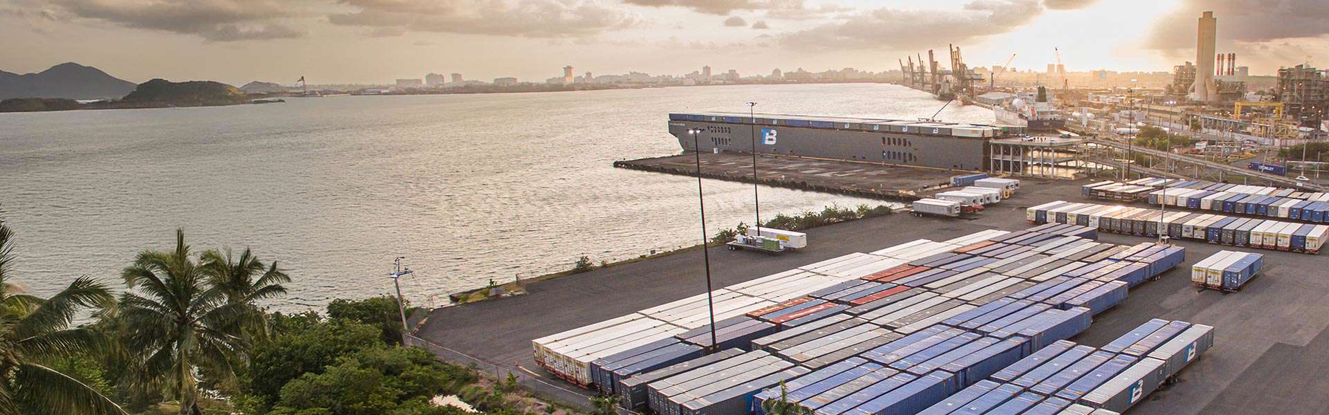 A Caribbean port with dozens of shipping containers and a large structure with the Trailer Bridge logo.