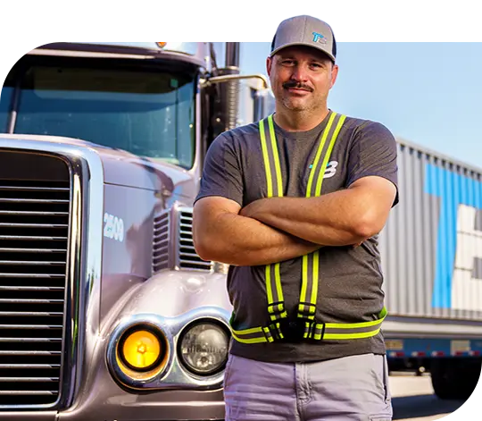 A Trailer Bridge employee stands next to a semi-truck with the Trailer Bridge logo.