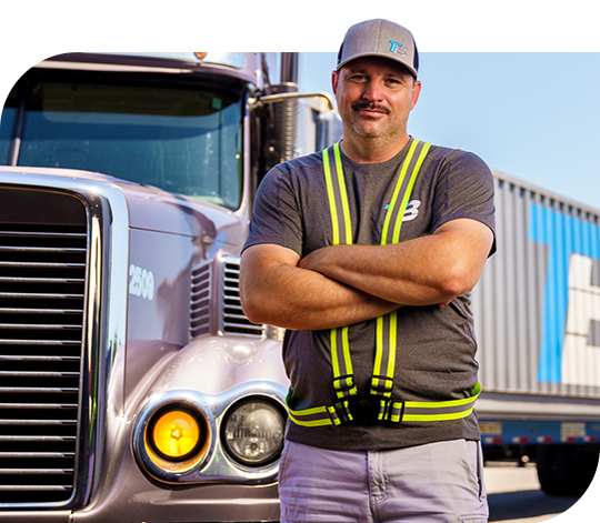 A Trailer Bridge employee stands next to a semi-truck with the Trailer Bridge logo.