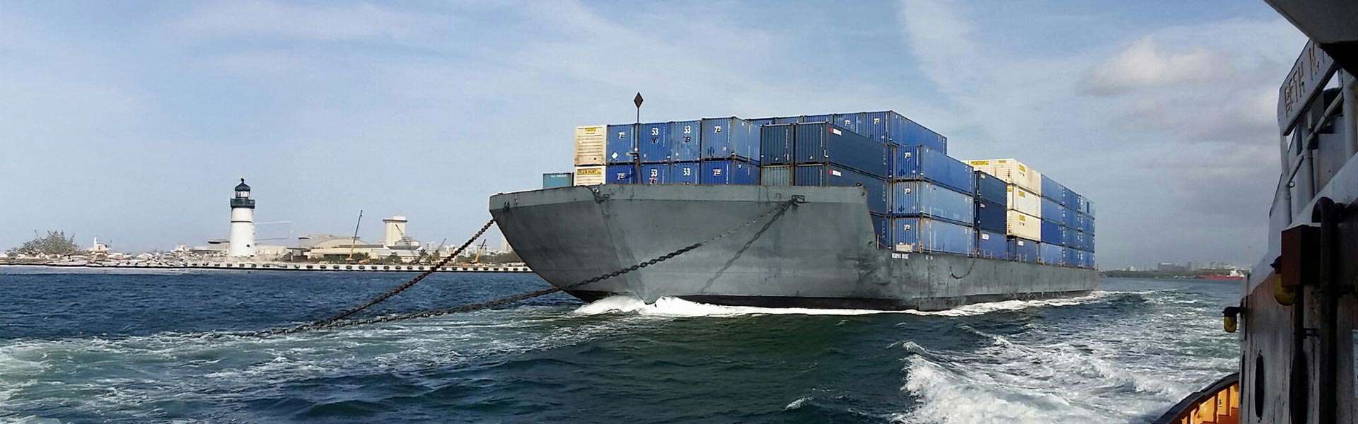 A barge leaves port with stacks of shipping containers.