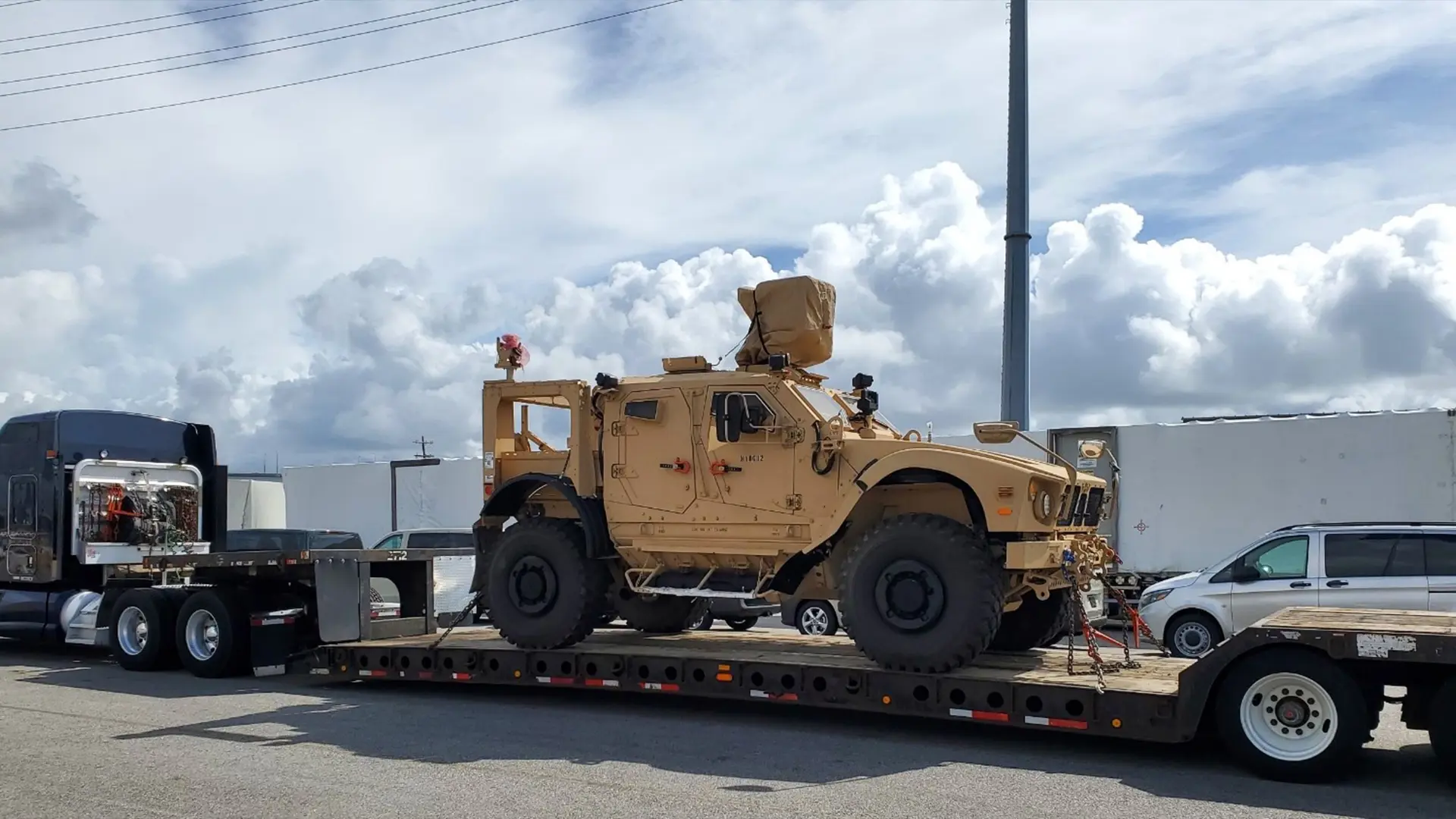 A military vehicle is chained onto a flatbed truck for transport.
