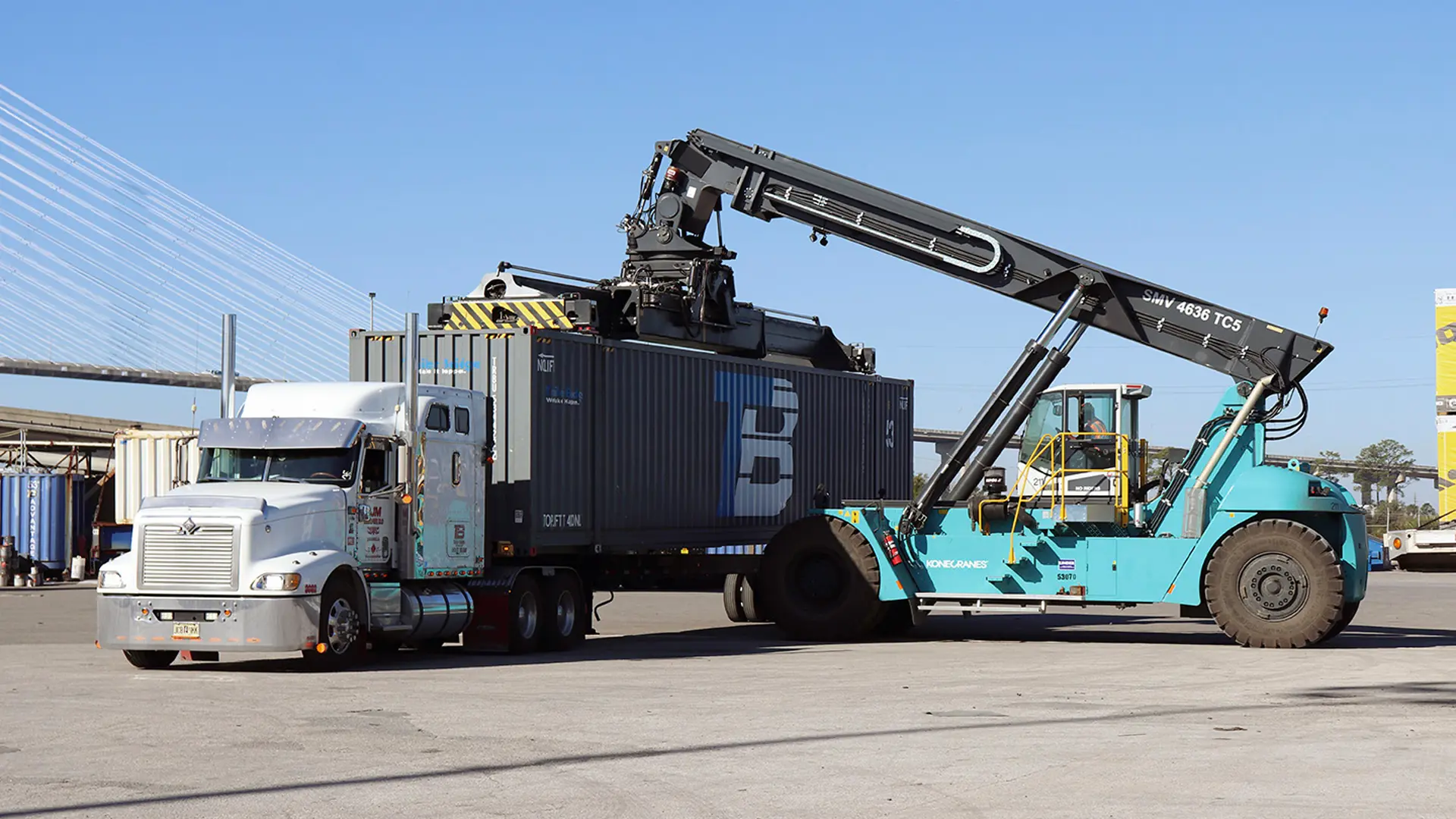 A crane vehicle moves a shipping container on or off a truck bed.