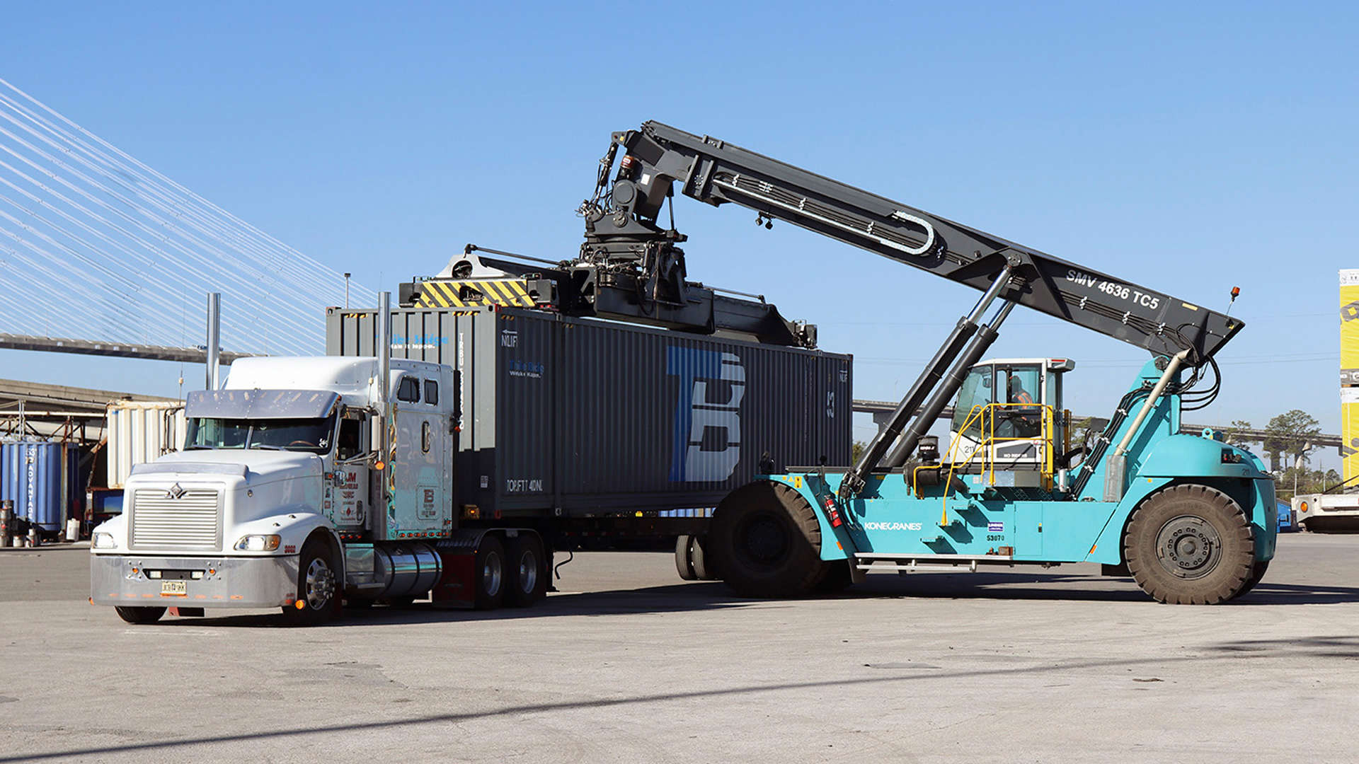 A crane vehicle moves a shipping container on or off a truck bed.