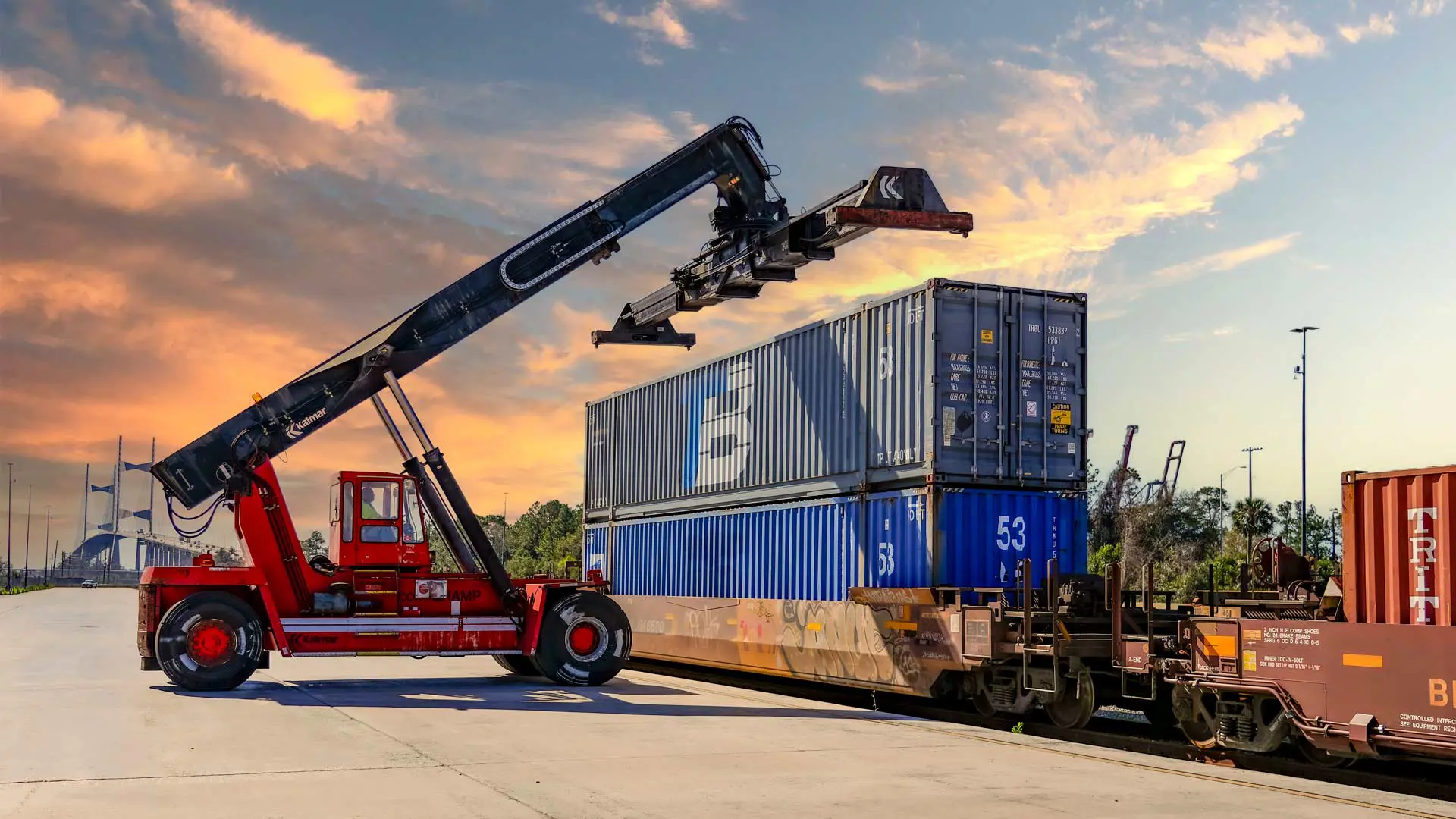 A crane vehicle lines up to move a shipping container off a train.