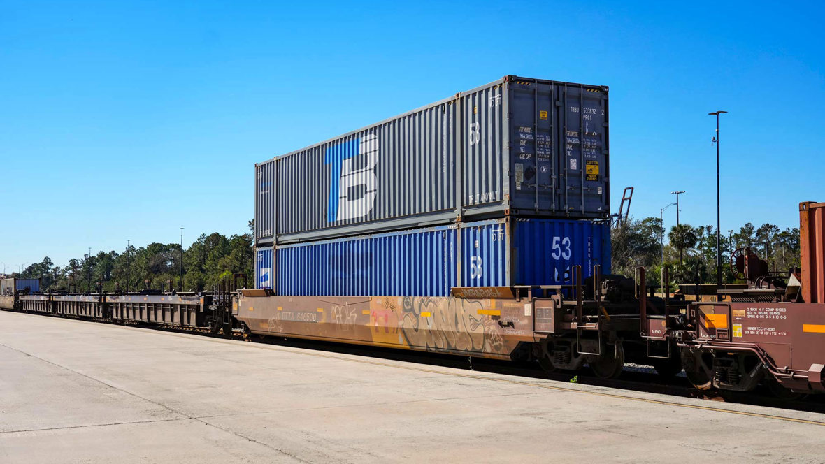 Two Trailer Bridge-branded containers stacked on each other being transported by rail.
