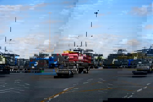 A flatbed truck transports large equipment out of a container area.