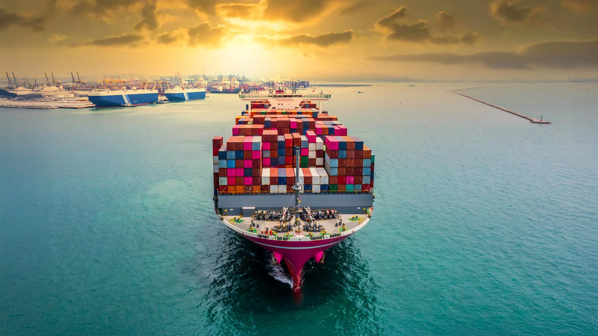 International shipping vessel sailing from port at sunset.