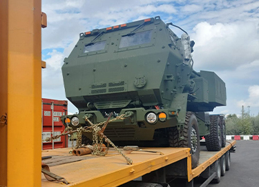 A large military vehicle is secured on the flatbed of a truck.