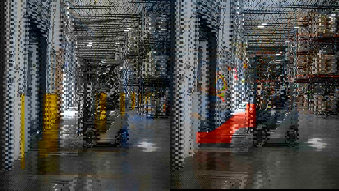 A forklift operator drives inside a warehouse.
