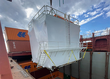 Scaffolded equipment being transported or stored amongst shipping containers.