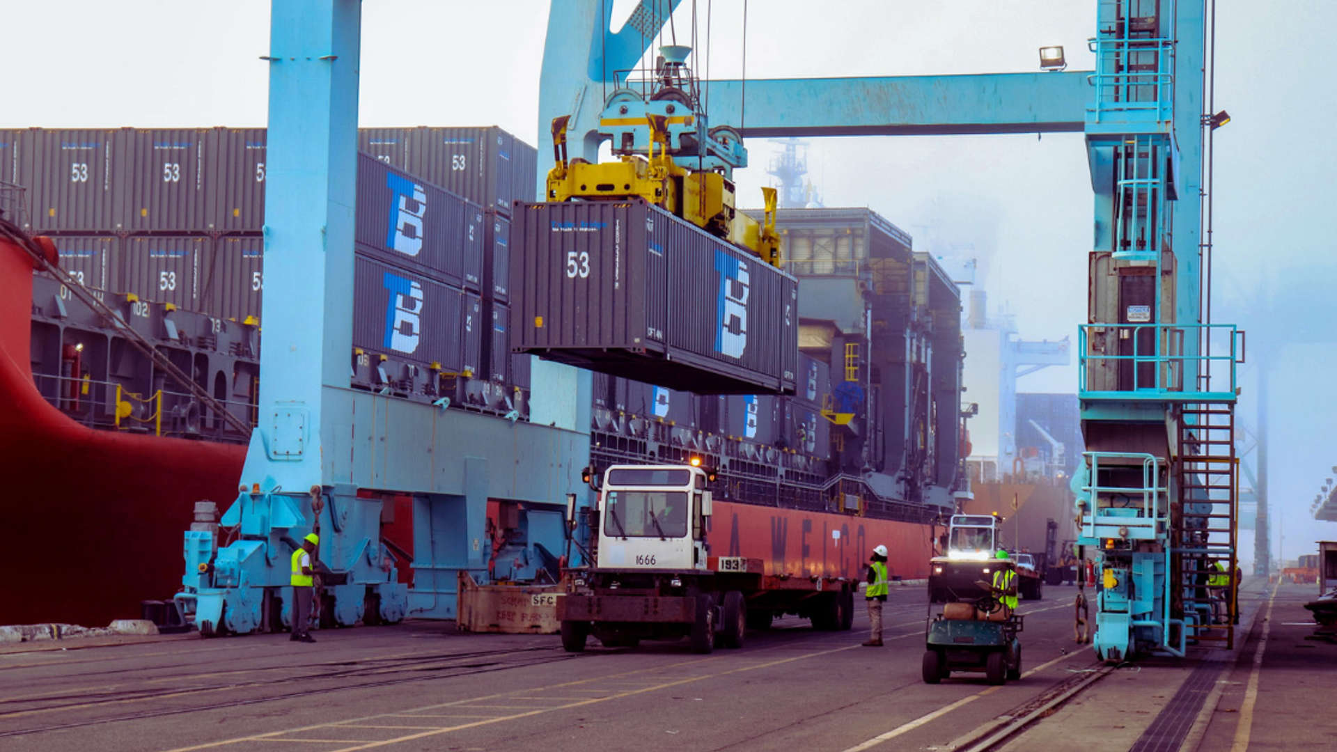 A crane lifts a container off a truck.