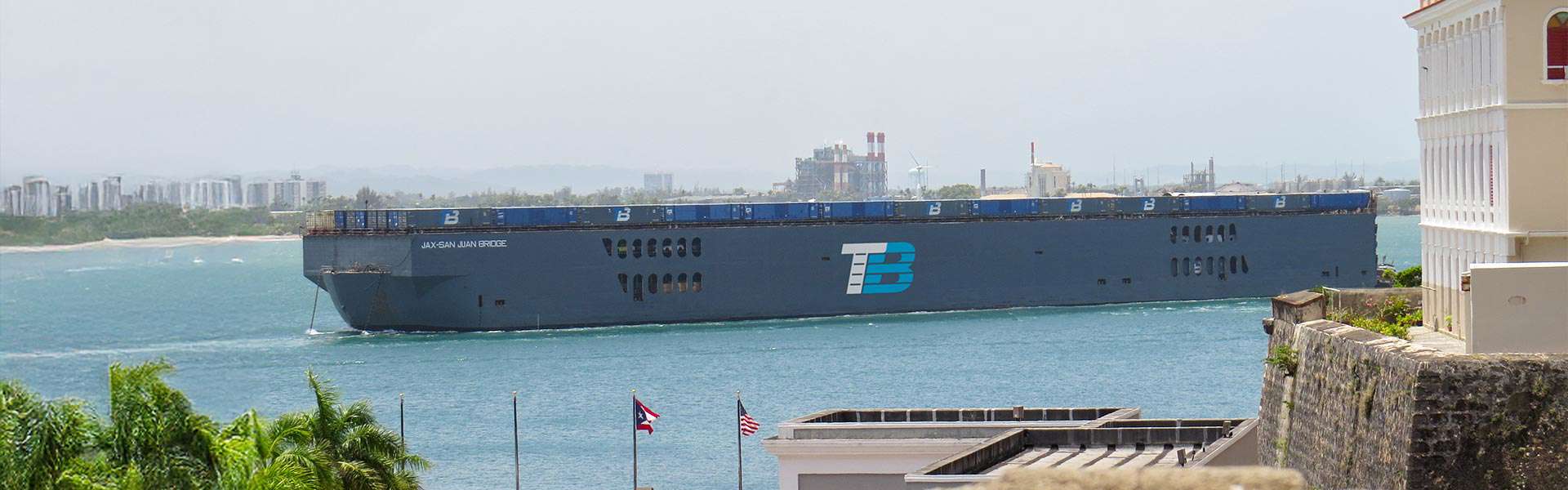 A barge with the Trailer Bridge logo carries shipping containers out of port.
