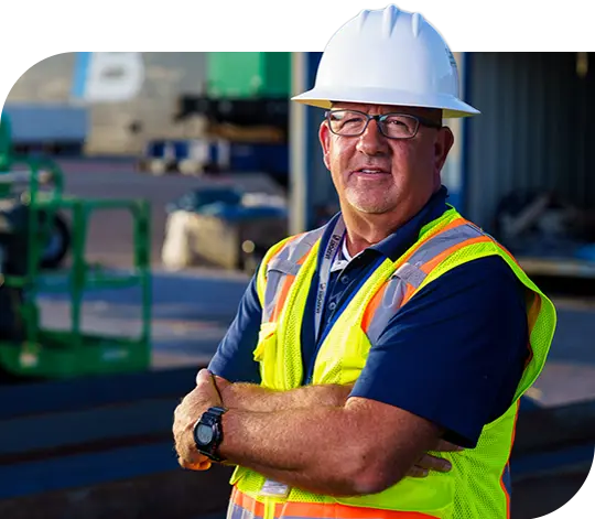 A Trailer Bridge employee wearing a hard hat and high visibility jacket stands with arms crossed.