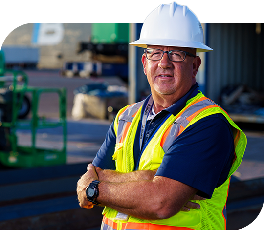 A Trailer Bridge employee wearing a hard hat and high visibility jacket stands with arms crossed.