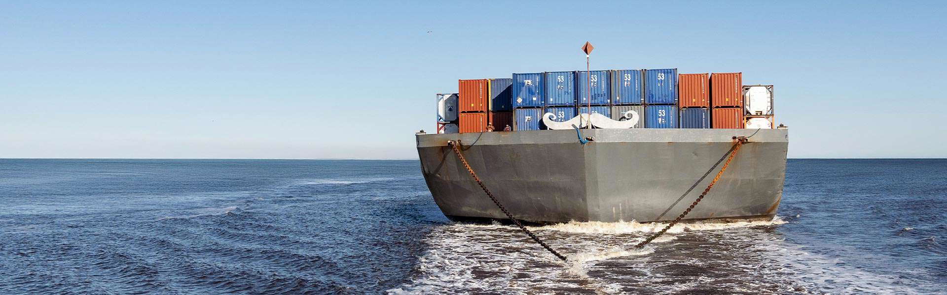 A barge on the ocean carries stacks of shipping containers.