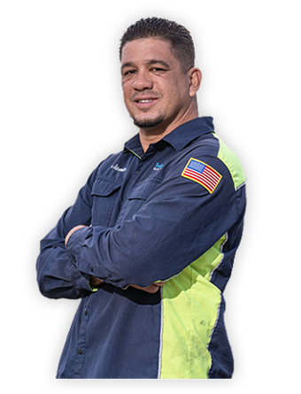 A Trailer Bridge employee in a jumpsuit stands with arms crossed.