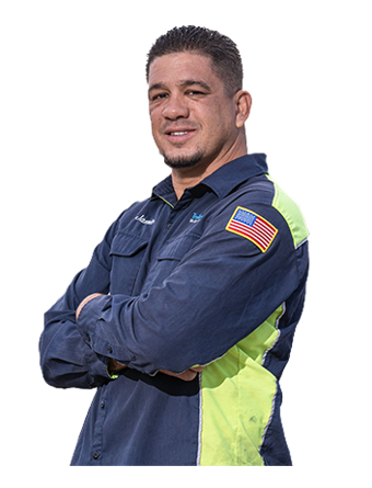 A Trailer Bridge employee in a jumpsuit stands with arms crossed.