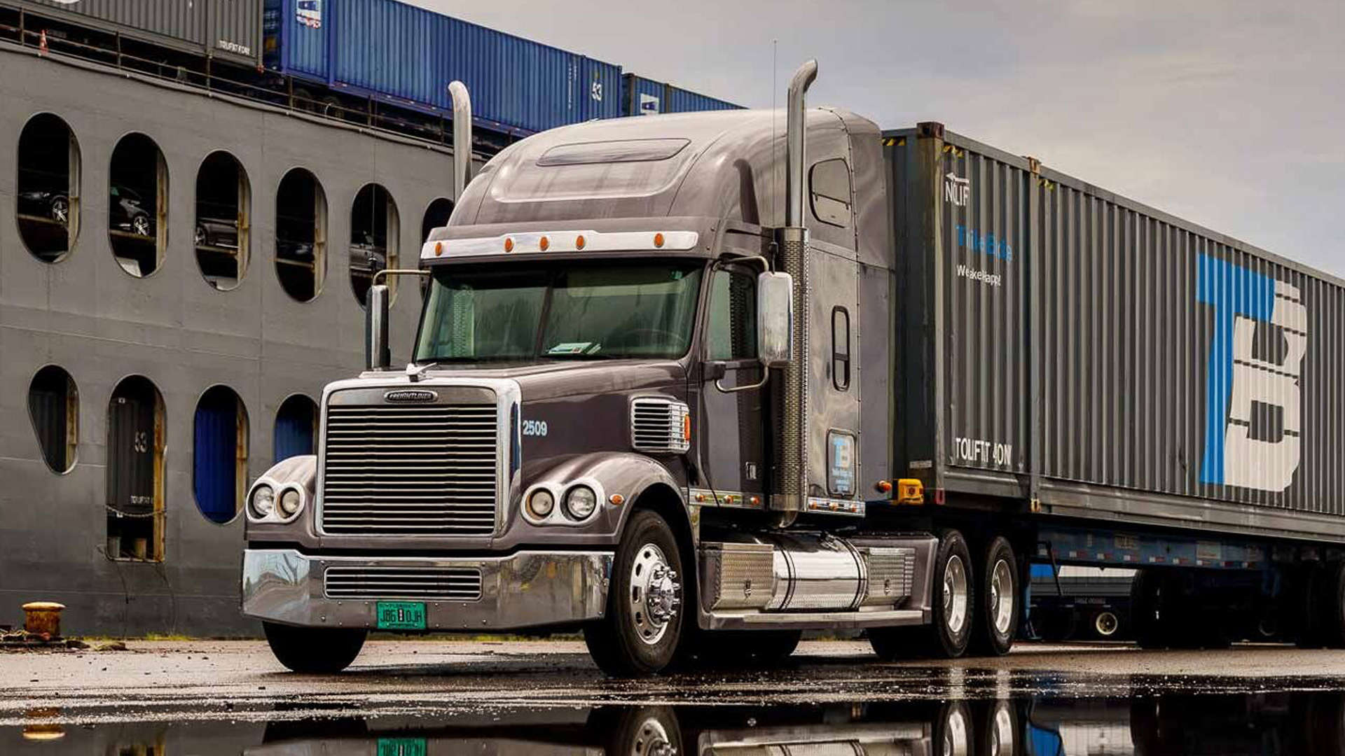 A large semi-truck with Trailer Bridge branding is parked outside a shipping storage facility.