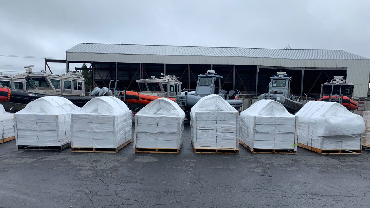 Several large, plastic-wrapped pieces of cargo are lined up at a port.