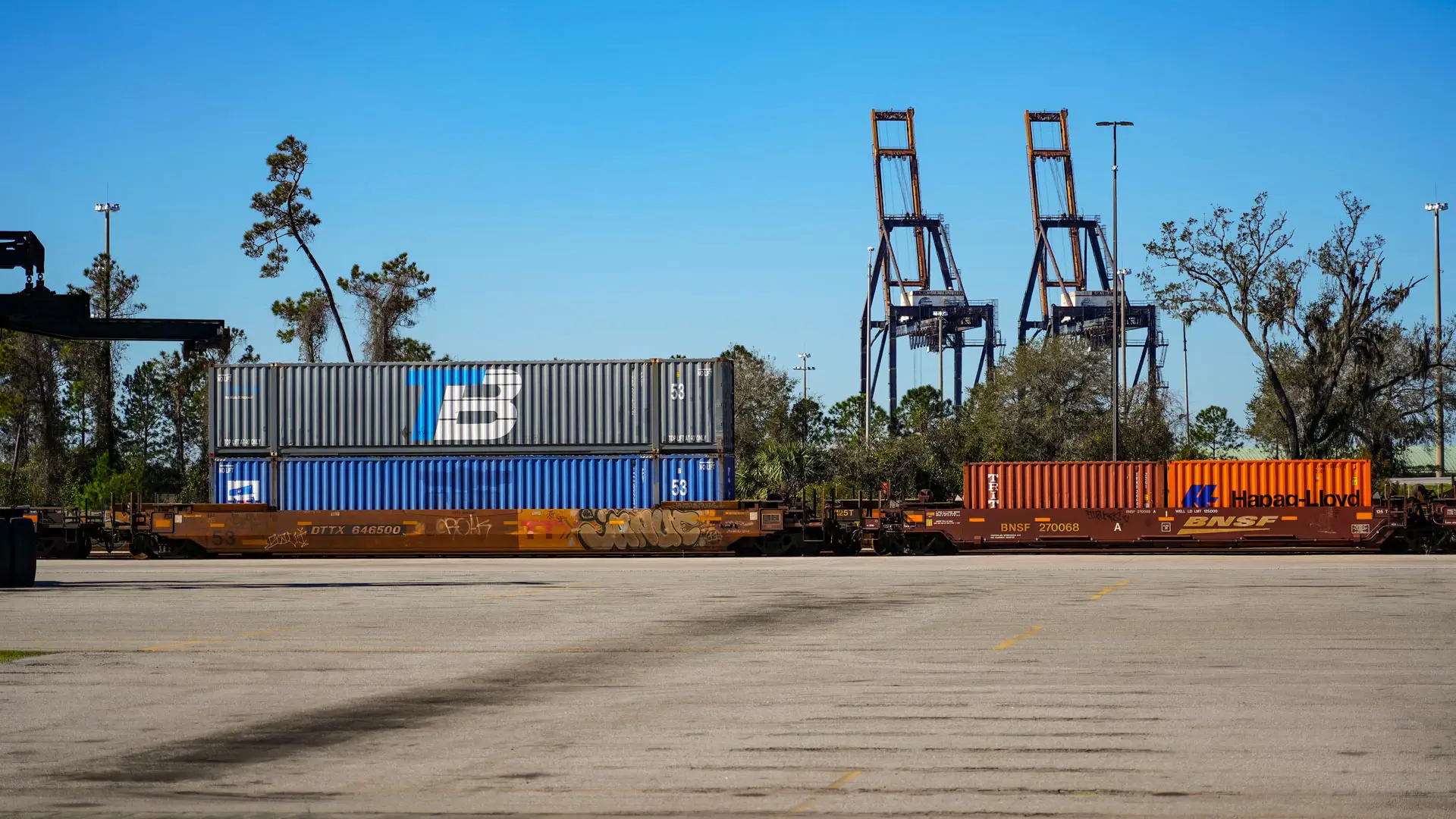 Several shipping containers being transported on a train, some of them with the Trailer Bridge logo.