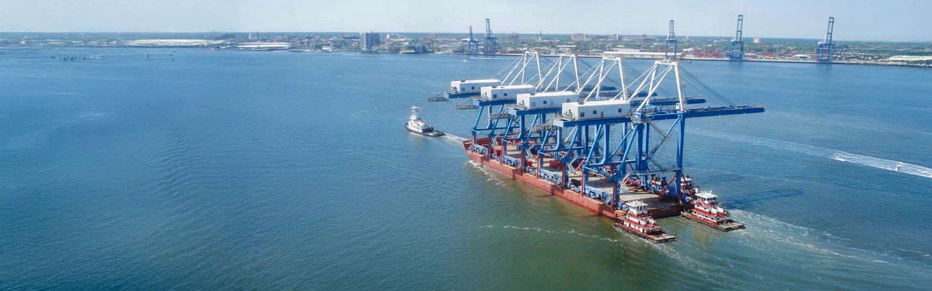 In the foreground is a container crane with a boat sailing away. A port is in the background.