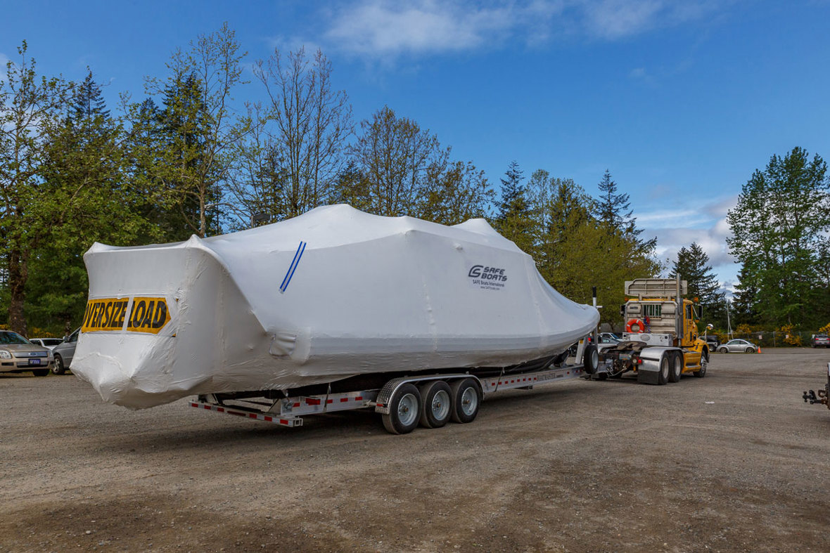A truck hauls a plastic-wrapped boat labeled "oversize load".