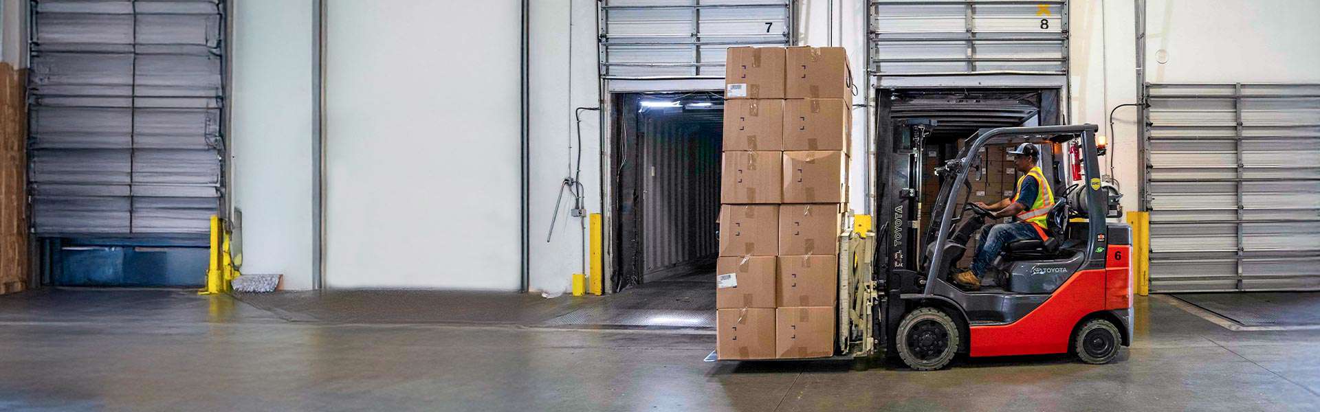 A forklift operator transports a stack of boxes across a warehouse.