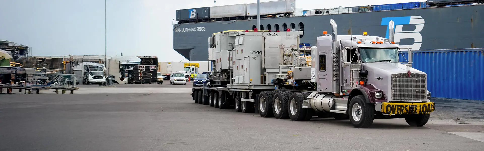 A truck with an "oversized load" banner transports boxes and equipment.