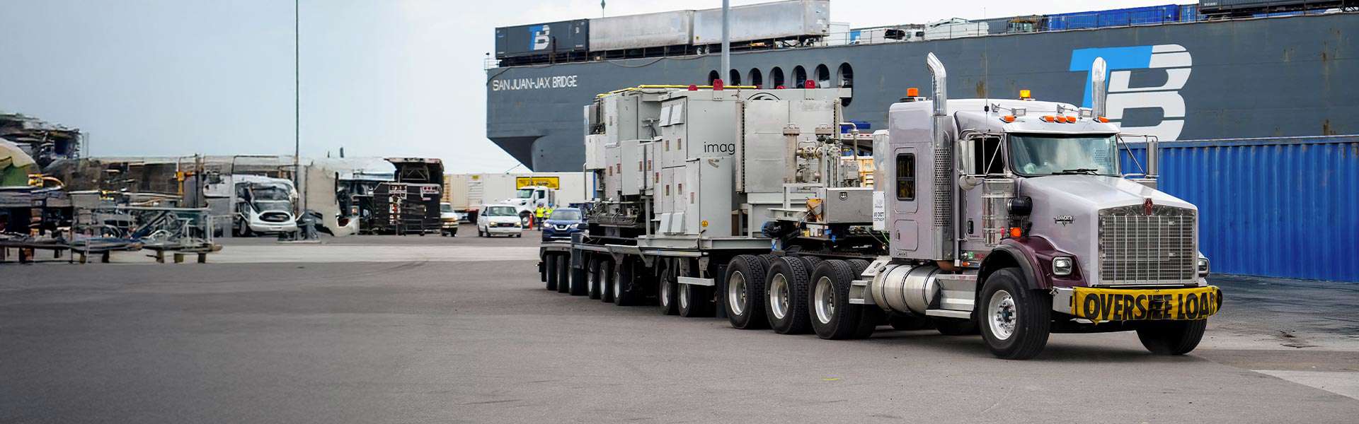 A truck with an "oversized load" banner transports boxes and equipment.