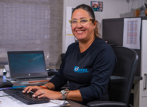Trailer Bridge employee smiles at camera, sitting at a desk with hands on a keyboard.