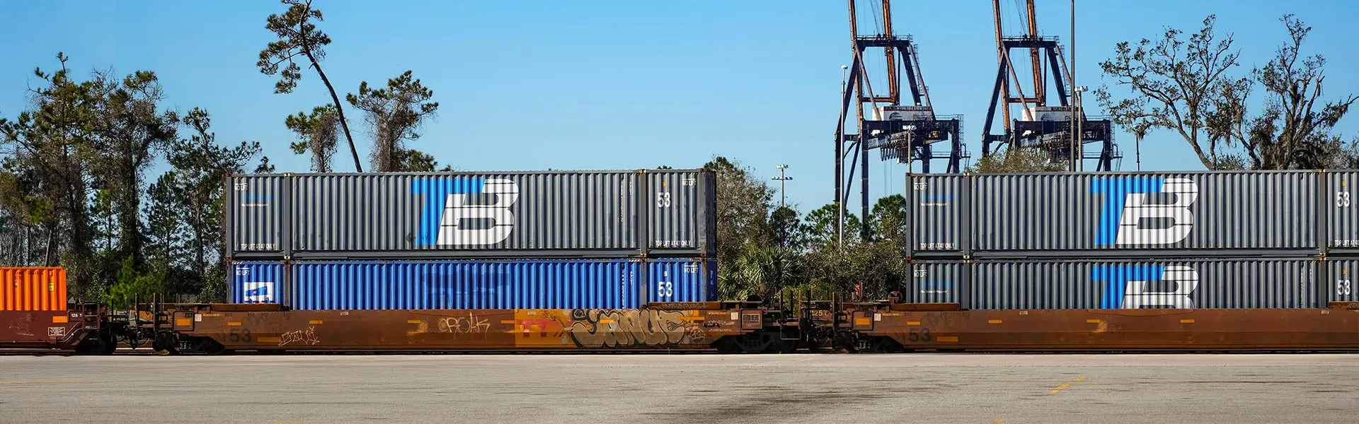 Several shipping containers being transported on a train, some of them with the Trailer Bridge logo.