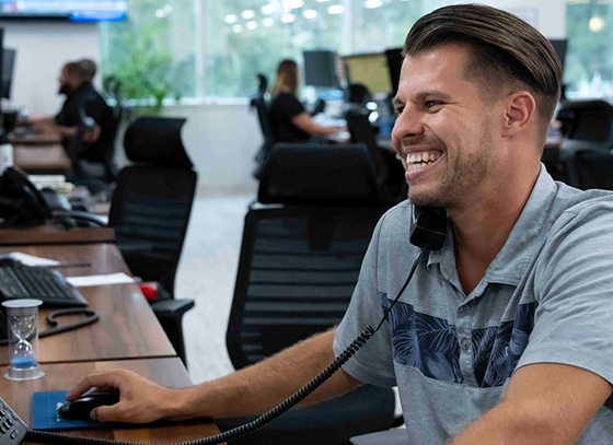 A smiling Trailer Bridge employee talks on the phone while also on a computer.