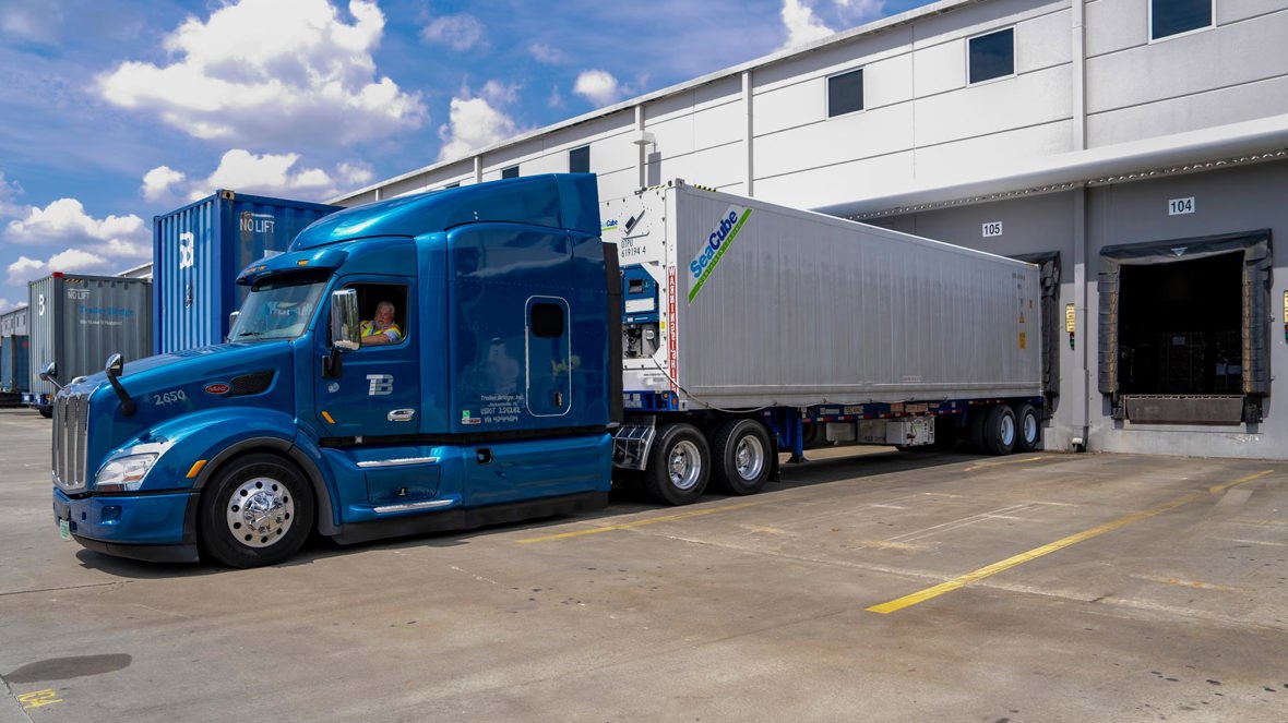A reefer trailer backs into a warehouse.