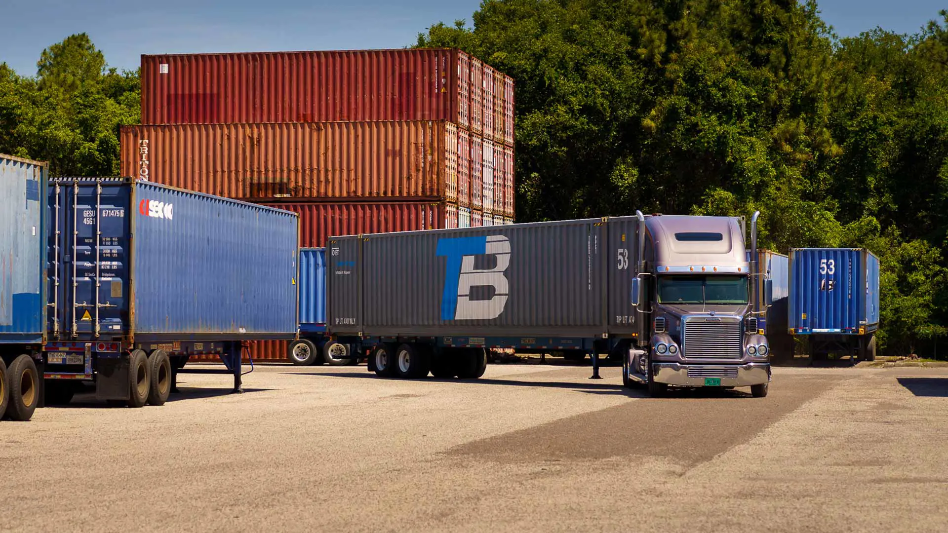 A Trailer Bridge truck pulls away from a lot of shipping containers.