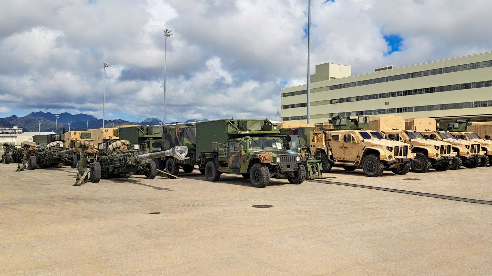 Lines of military vehicles are parked on concrete.