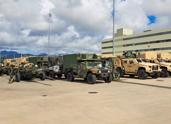 Lines of military vehicles are parked on concrete.