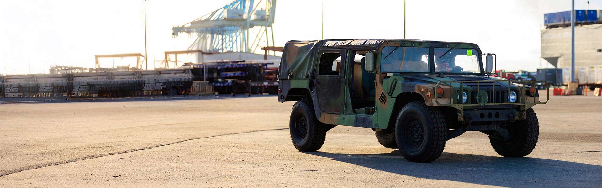 A camouflage-colored military Humvee sits parked at a port.