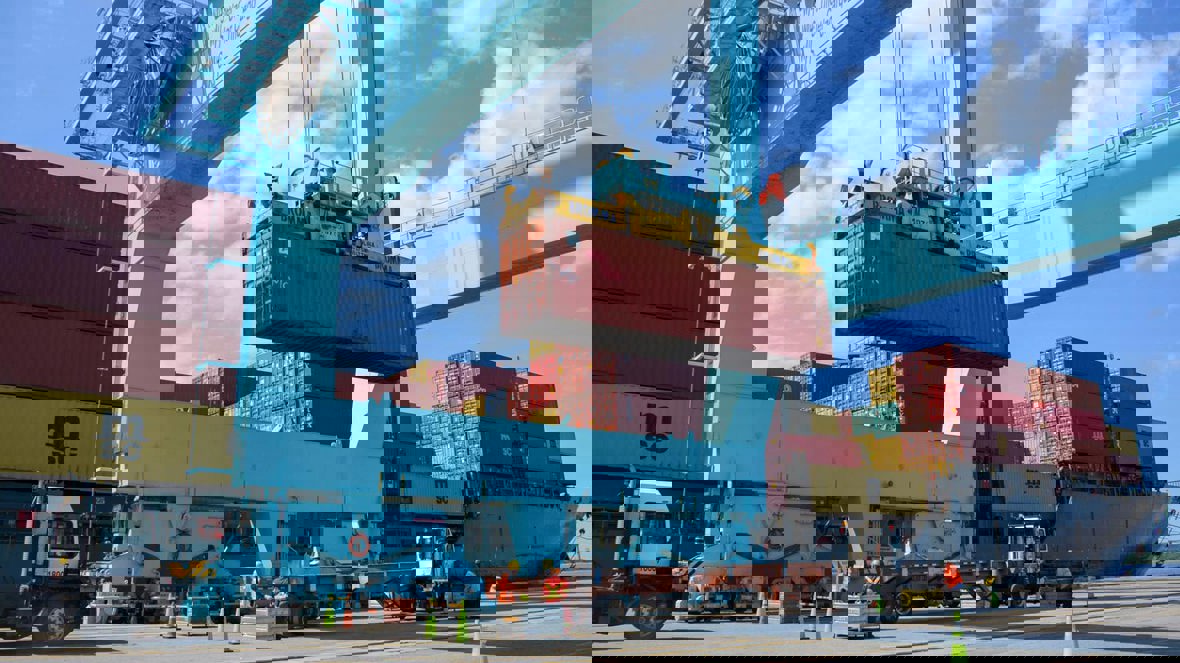A shipping container is being unloaded from a ship via crane.