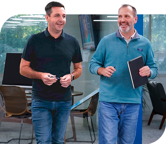 Two employees stand, talking, in an office.