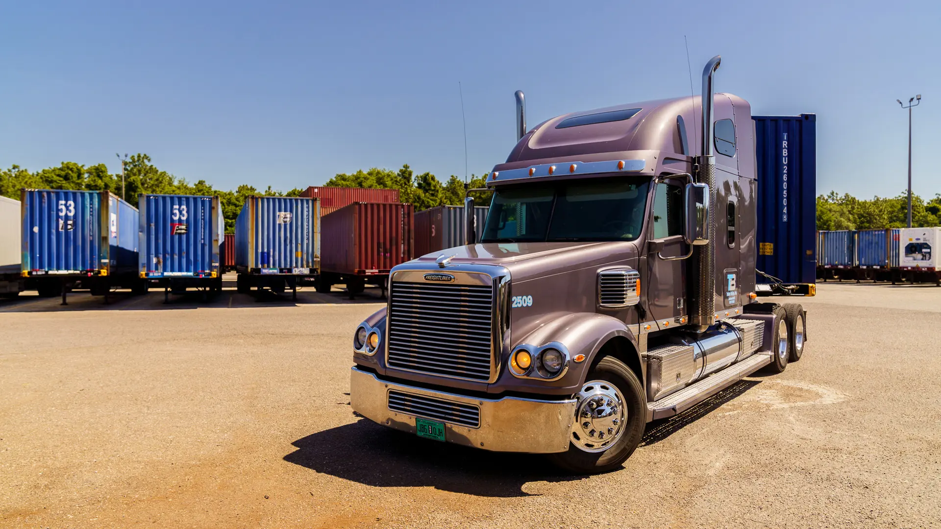 A Trailer Bridge truck without a trailer parked in front of trailers.