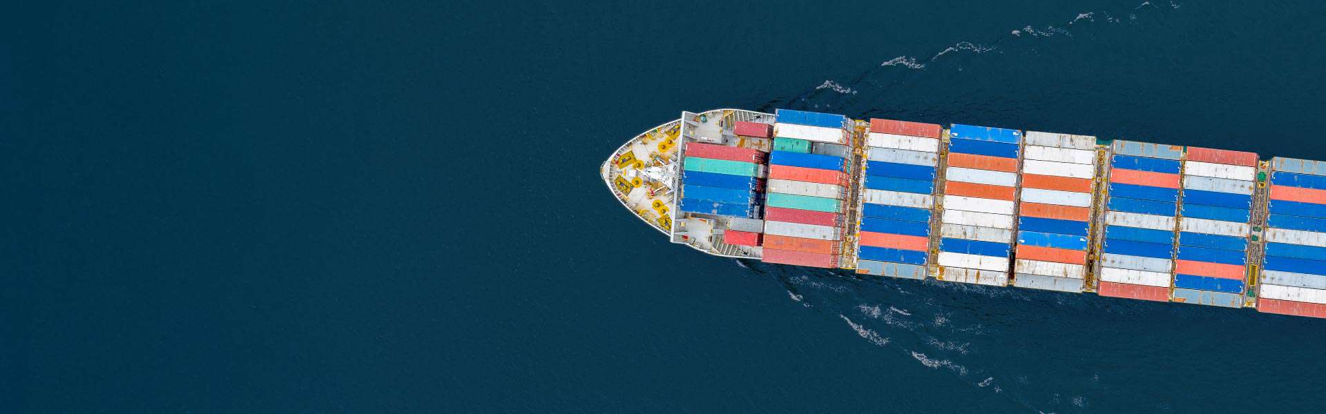 An overhead shot of a barge stacked with shipping containers in multiple colors.