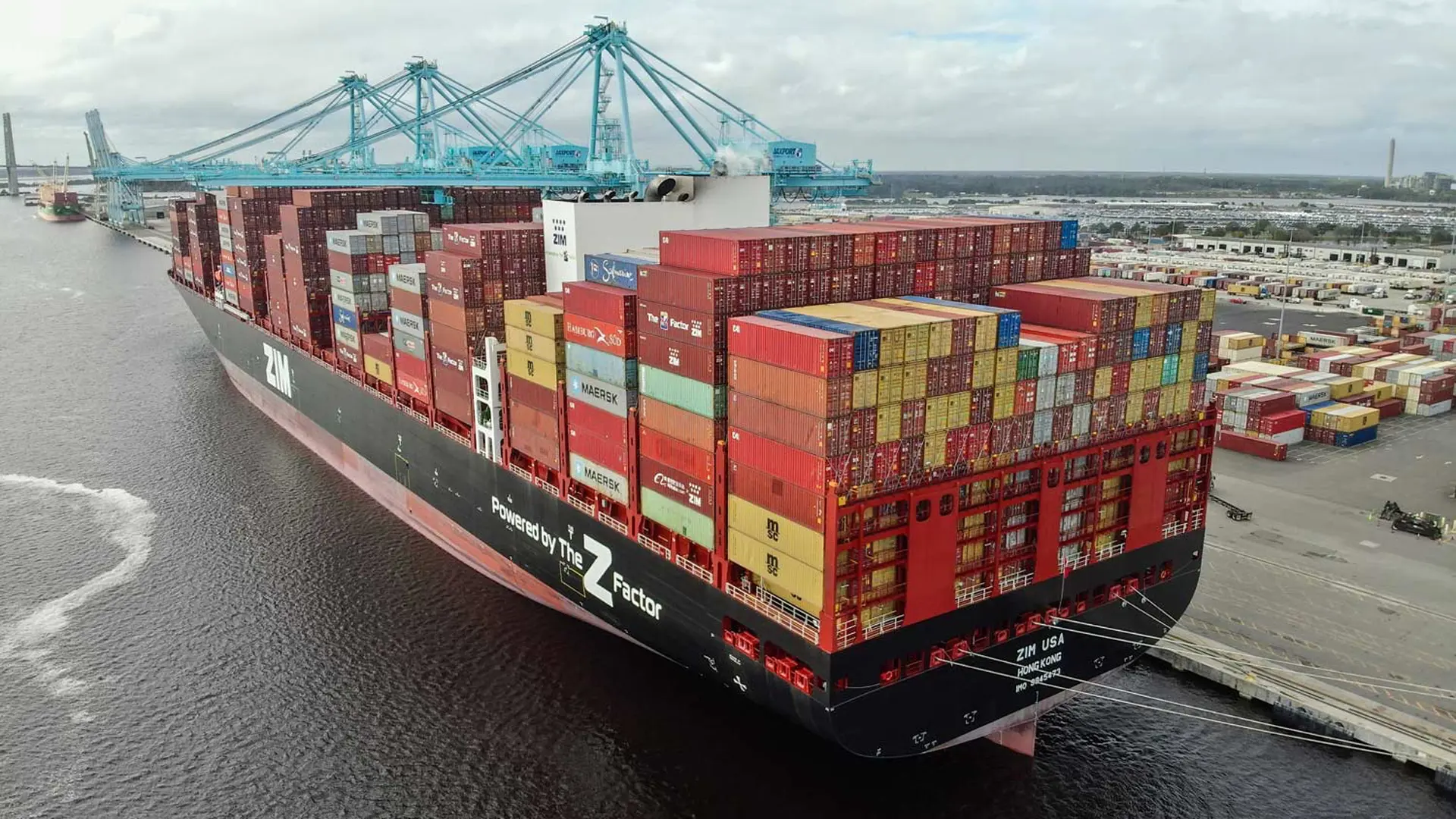 A barge stacked with shipping containers waits in a shipyard.