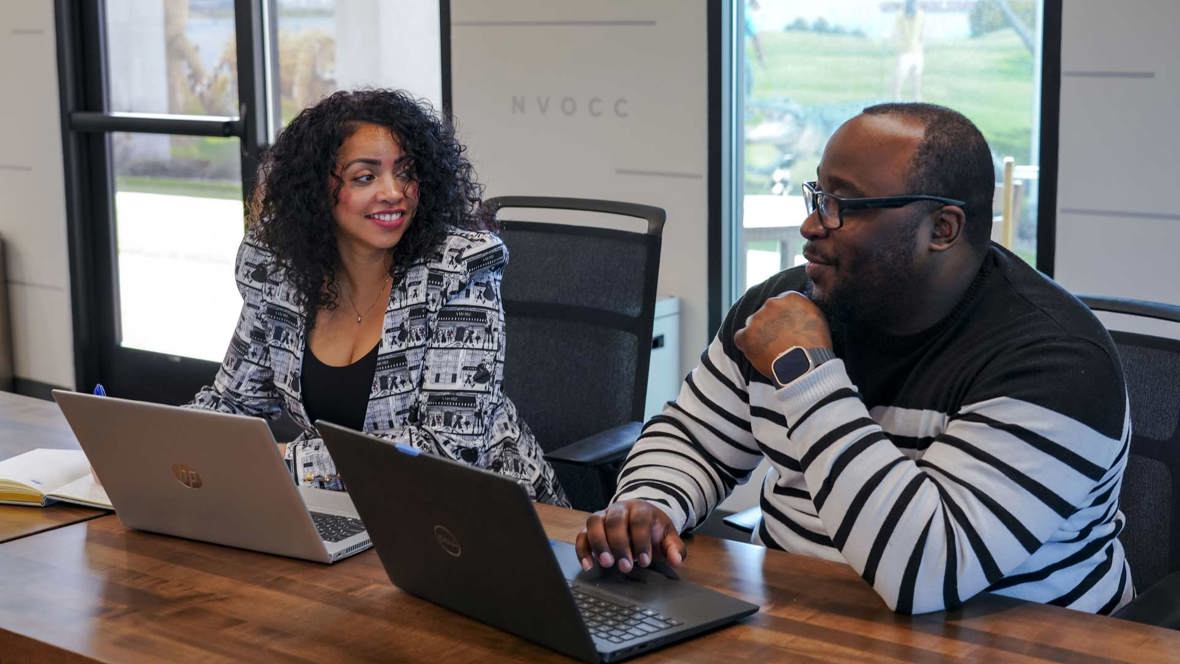 Two people sit with laptops on a table.
