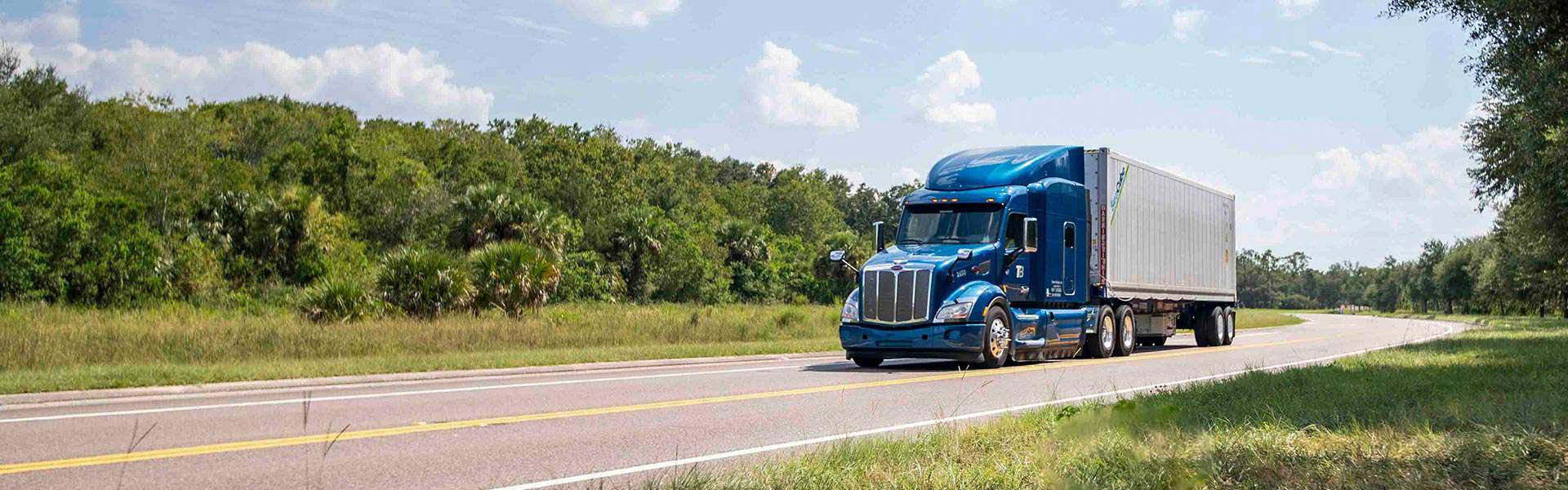 A Trailer Bridge semi-truck drives along a curving road.