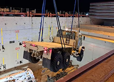 A crane moves a military vehicle within a warehouse.