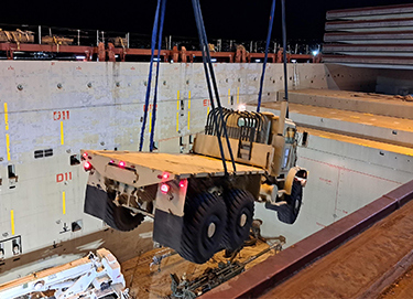 A crane moves a military vehicle within a warehouse.