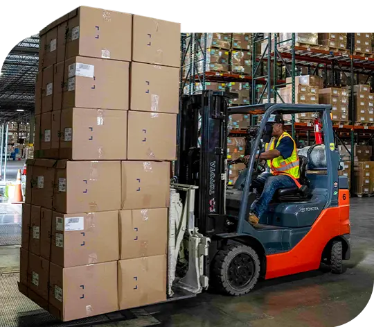 A forklift operator in a warehouse transports a tall stack of boxes.