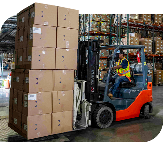 A forklift operator in a warehouse transports a tall stack of boxes.